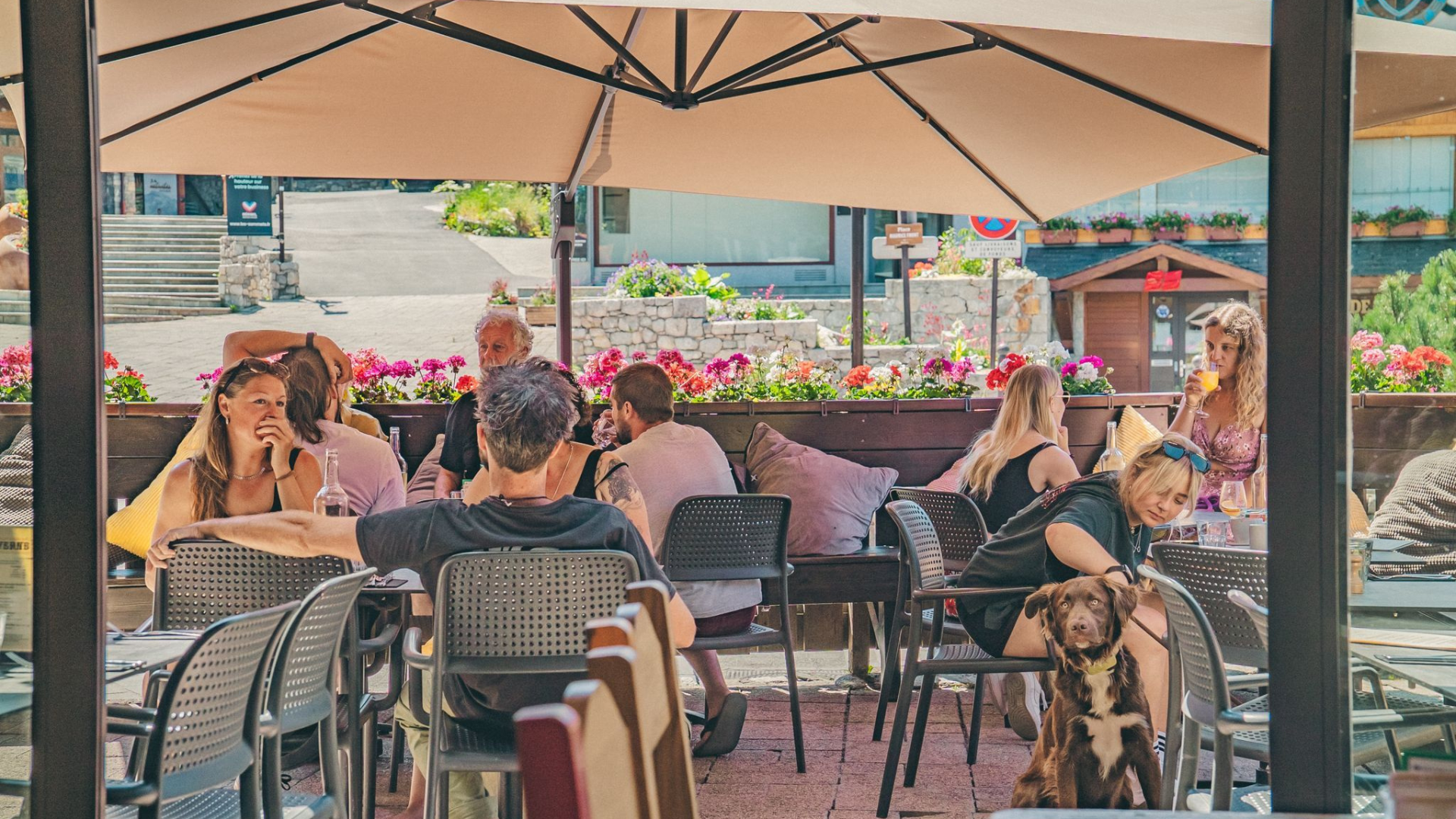 Lively outdoor dining terrace at La Taverne, a mountain restaurant in Méribel, filled with guests enjoying drinks in the summer sunshine.
